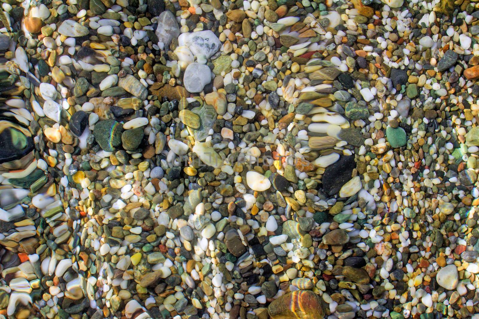 Small multi-colored sea stones on the beach, covered with transparent sea water.