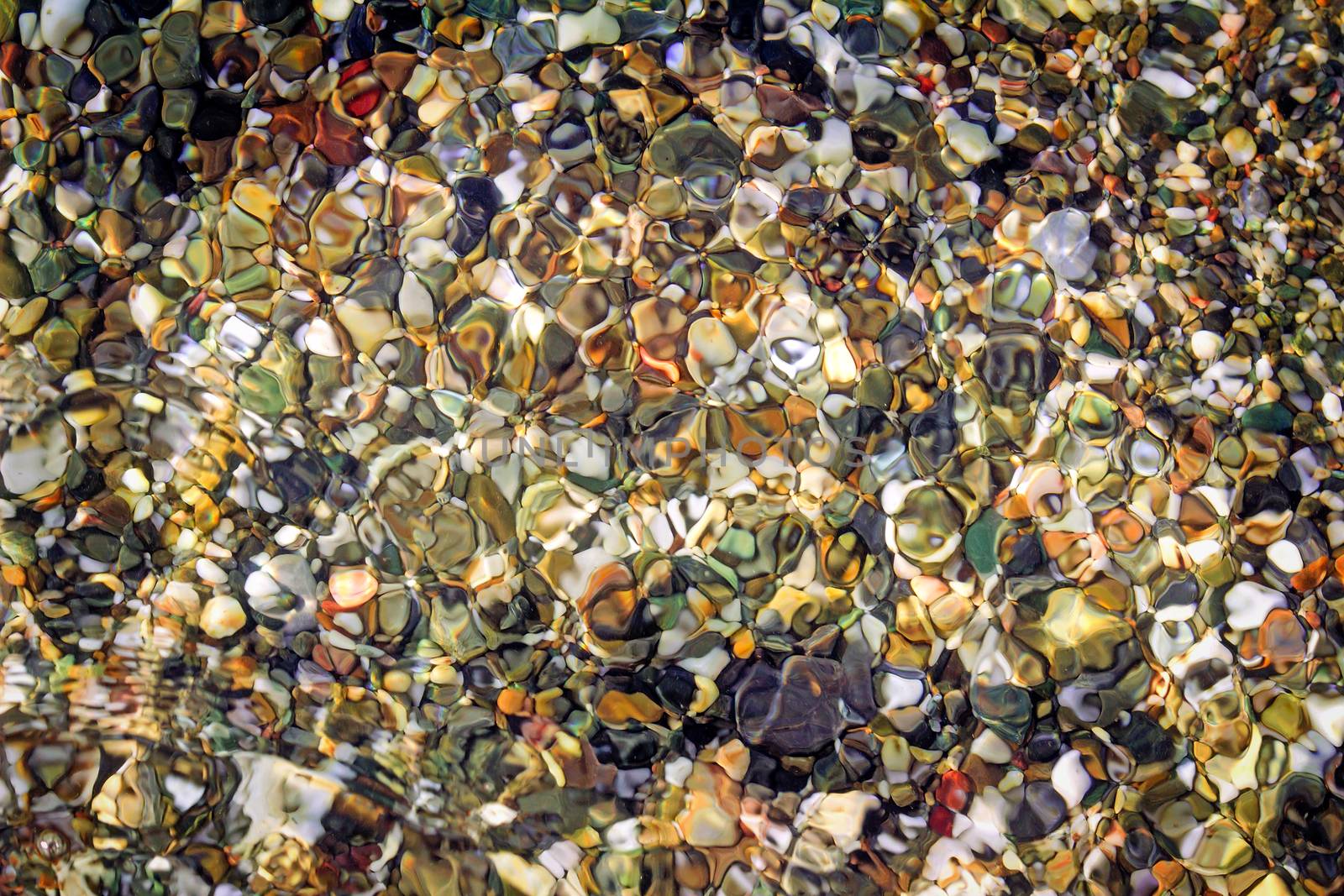 Small multi-colored sea stones on the beach, covered with transparent sea water.