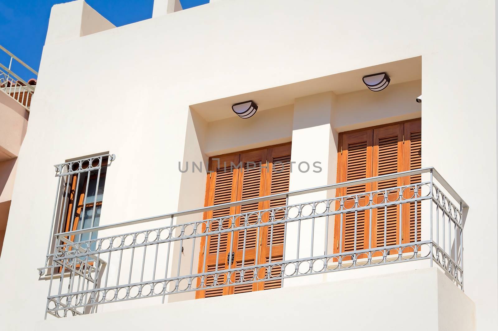 Fragment of a facade of the old house on the coast of the island of Crete with a balcony and ancient wooden blinds from the sun.