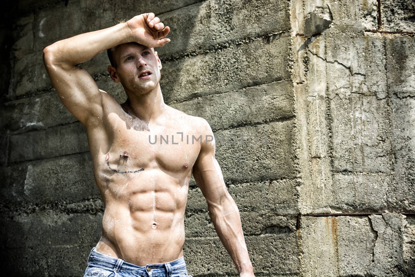 Handsome, muscular young construction worker shirtless outdoor, wiping off sweat from forehead