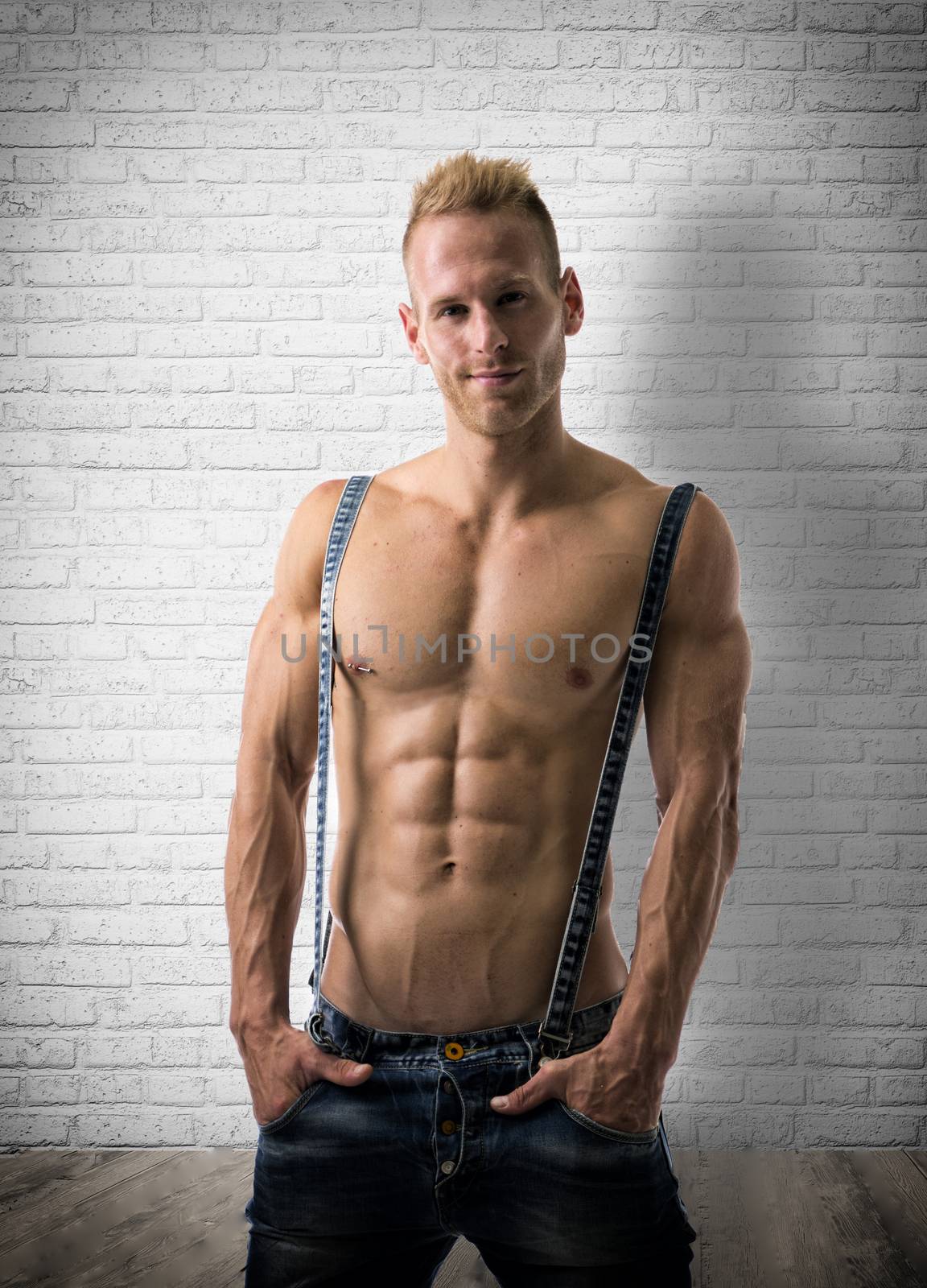 Sexy portrait of a very muscular blond shirtless male model smiling near brick wall