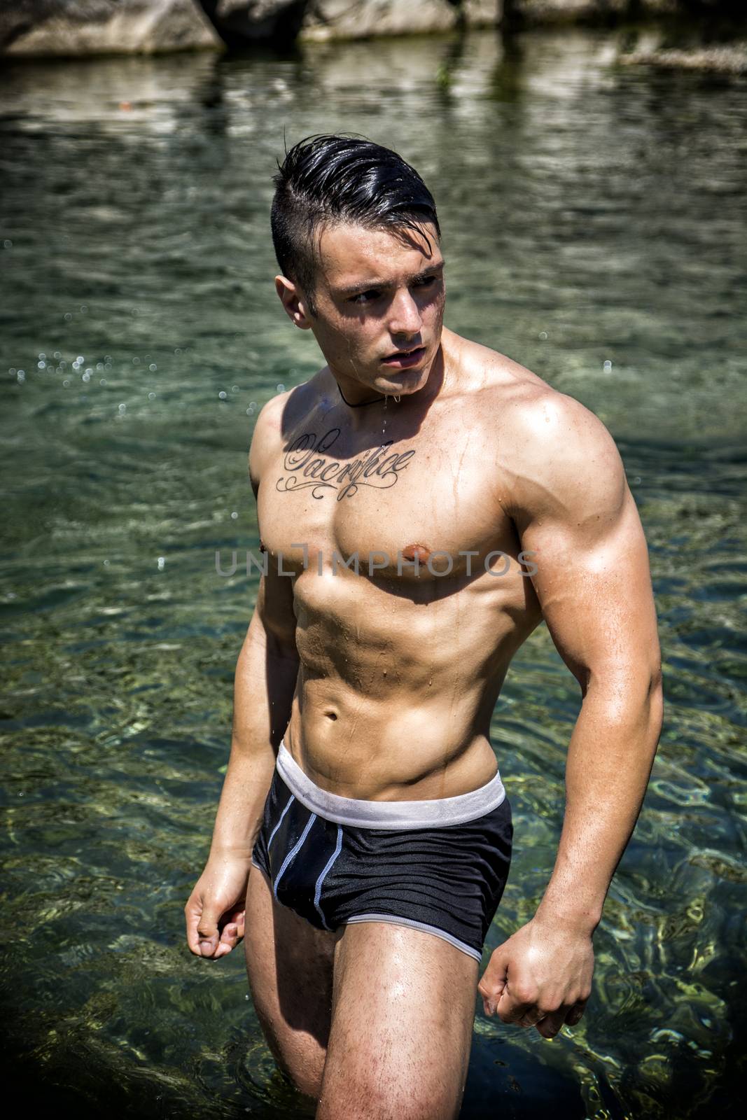 Handsome, hot young bodybuilder shirtless in trunks, in the sea showing his muscular torso and arms