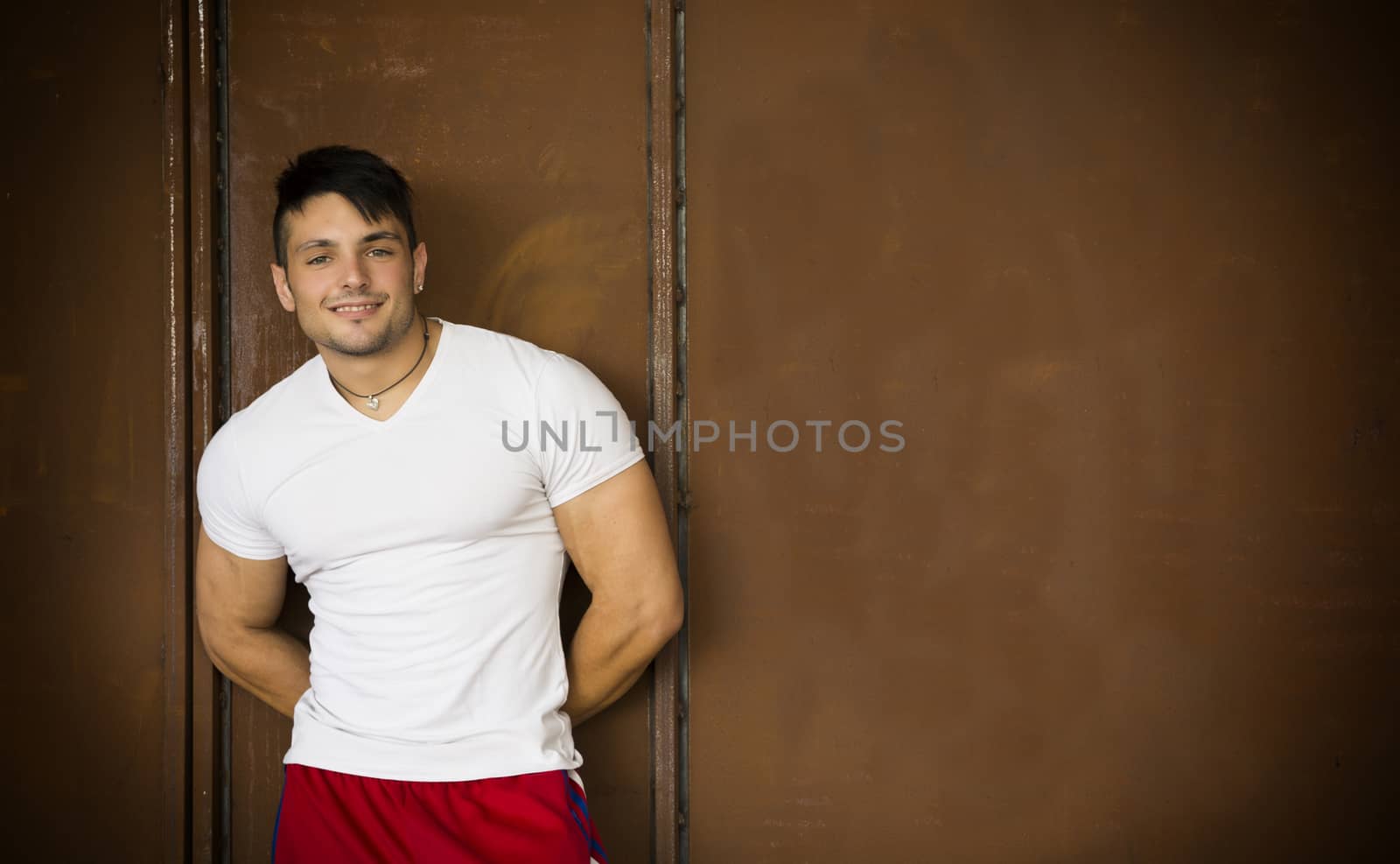 Muscular young man portrait indoors smiling at camera, wearing white t-shirt