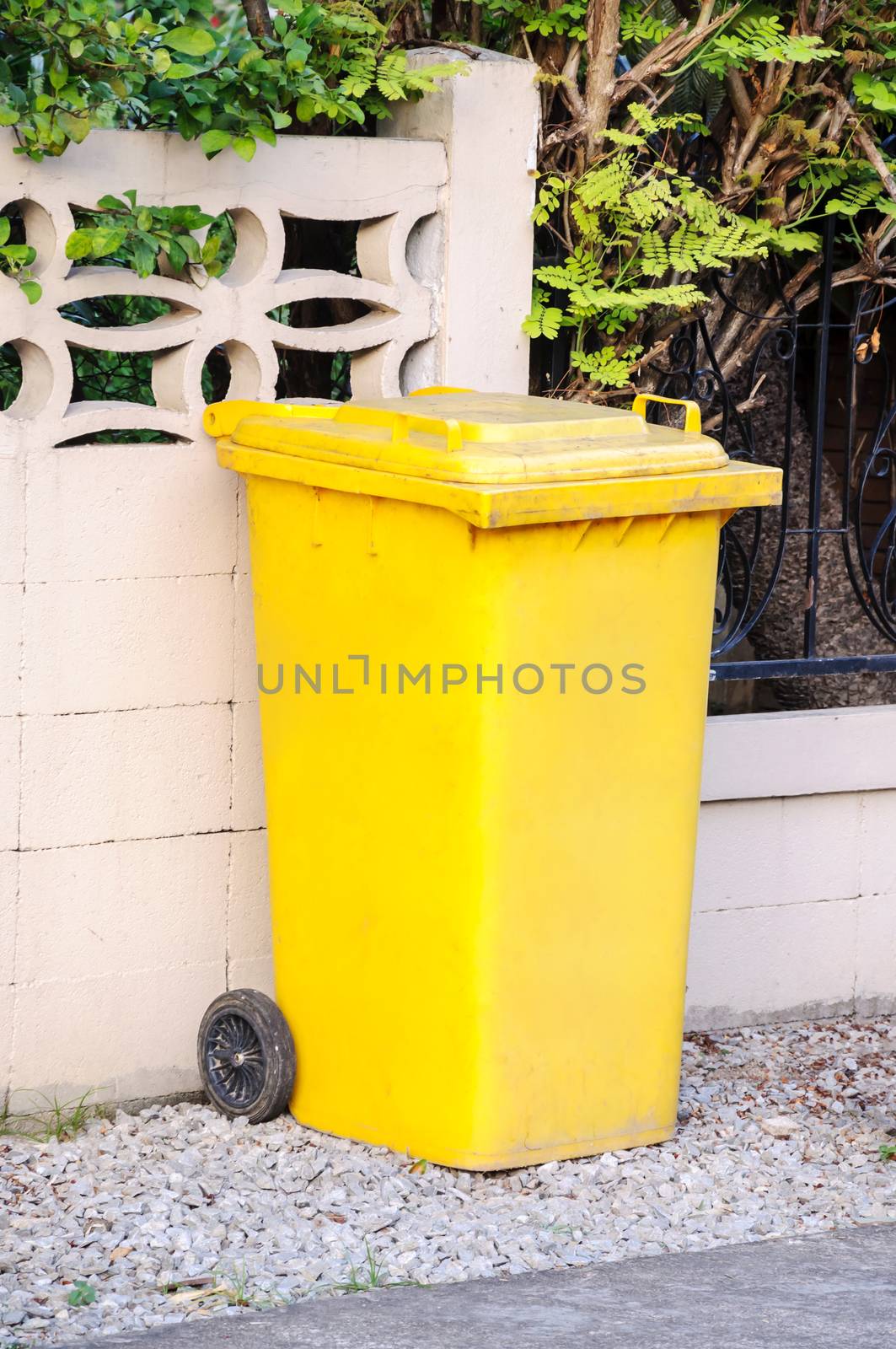 Yellow garbage, trash bin on side of the wall.