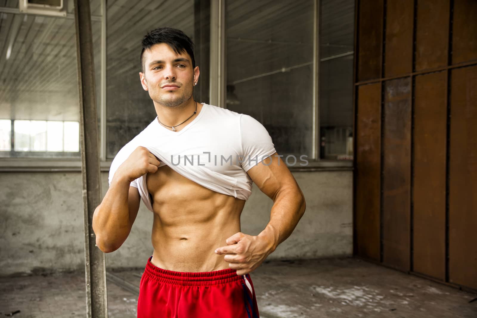 Attractive young muscular man portrait in white shirt and red shorts posing