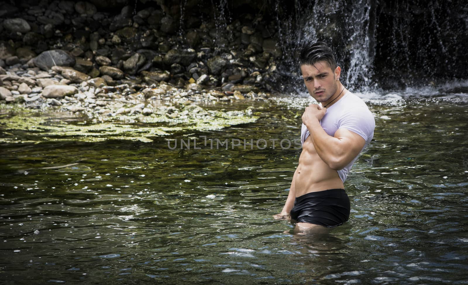 Handsome, hot young bodybuilder in the sea or river showing his muscular abs and arms