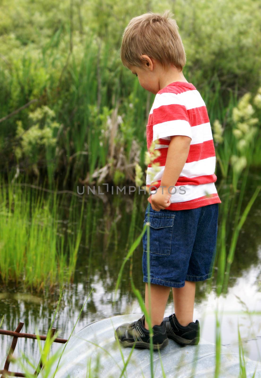 A happy two year old boy sparks curiousity at a nearby culvert while searching for tadpoles, frogs, and fish.