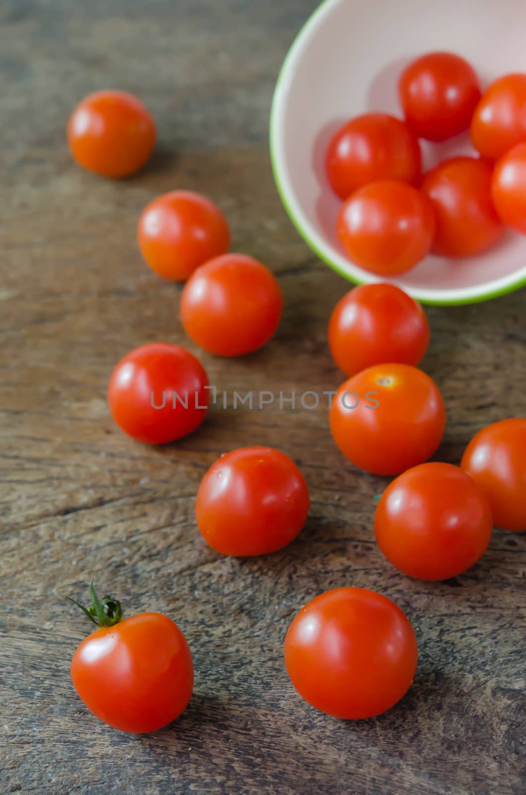 Red cherry tomatoes  spilling out from bowl on wooden background