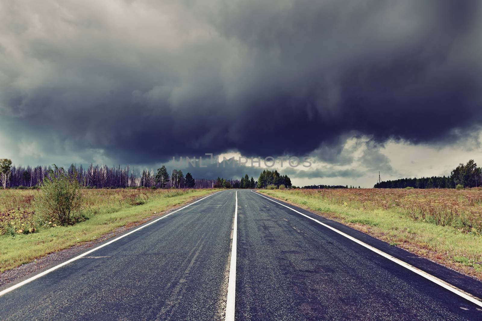 asphalt road and dark thunder clouds over it . 