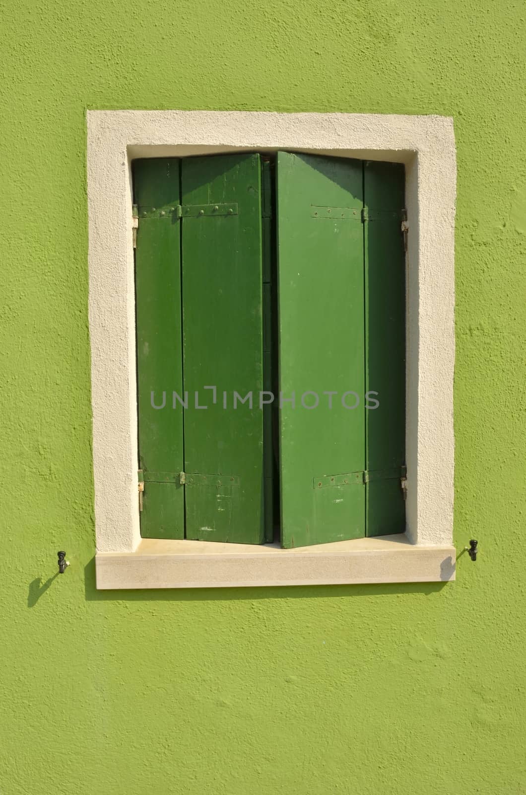 Green shutters on a vivid green wall in the island of Burano, Venice, Italy
