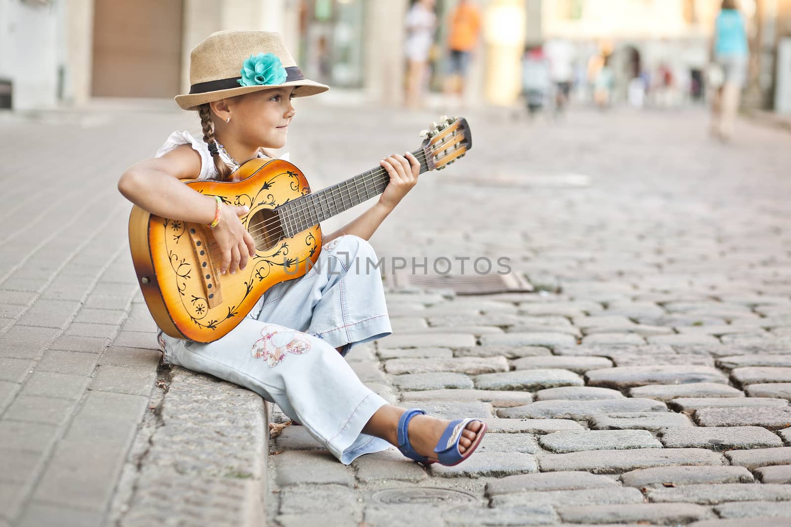 Small infant girl playing guitar on the city street