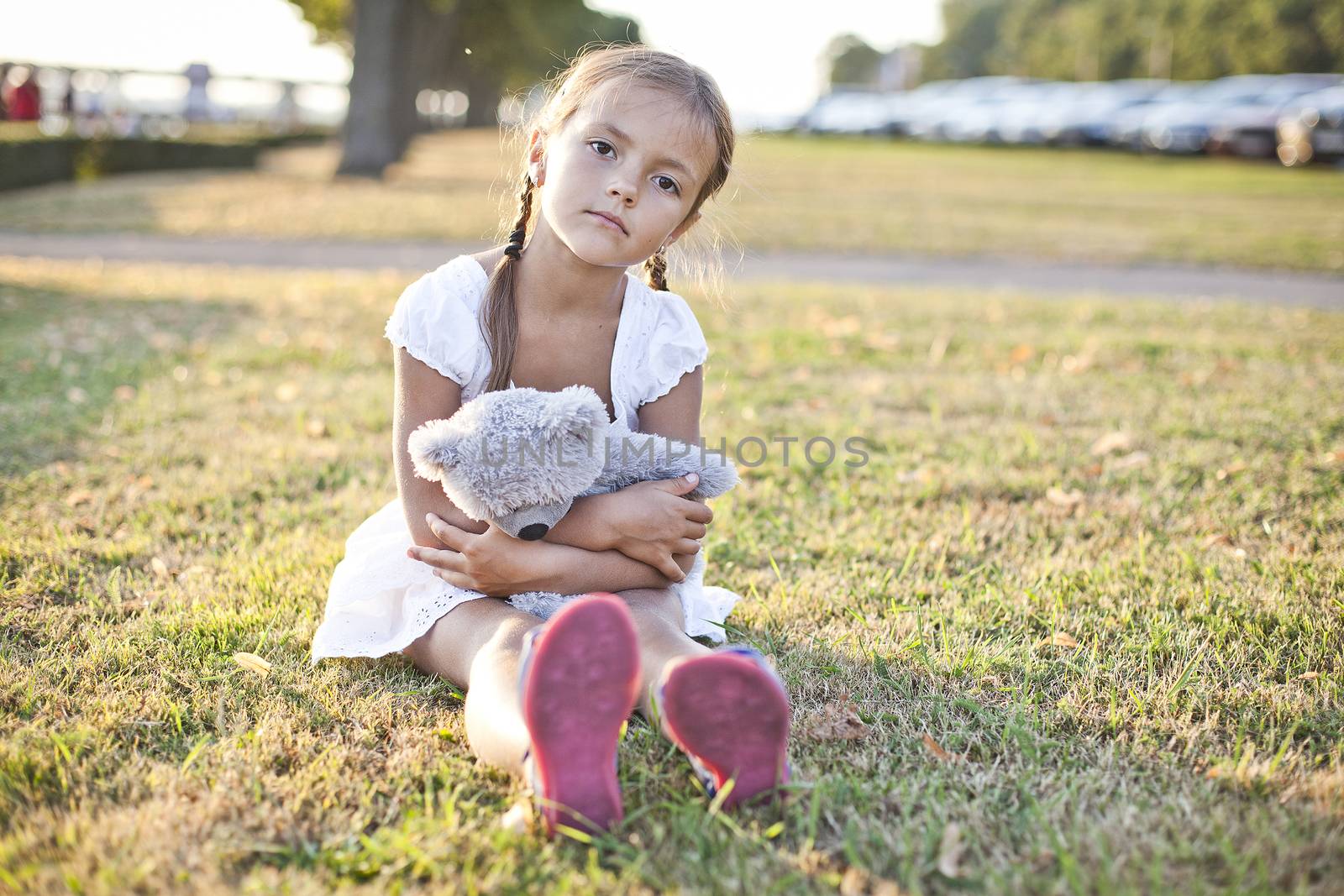 Young lonely girl sit on a grass in a park with her toy teddy bear