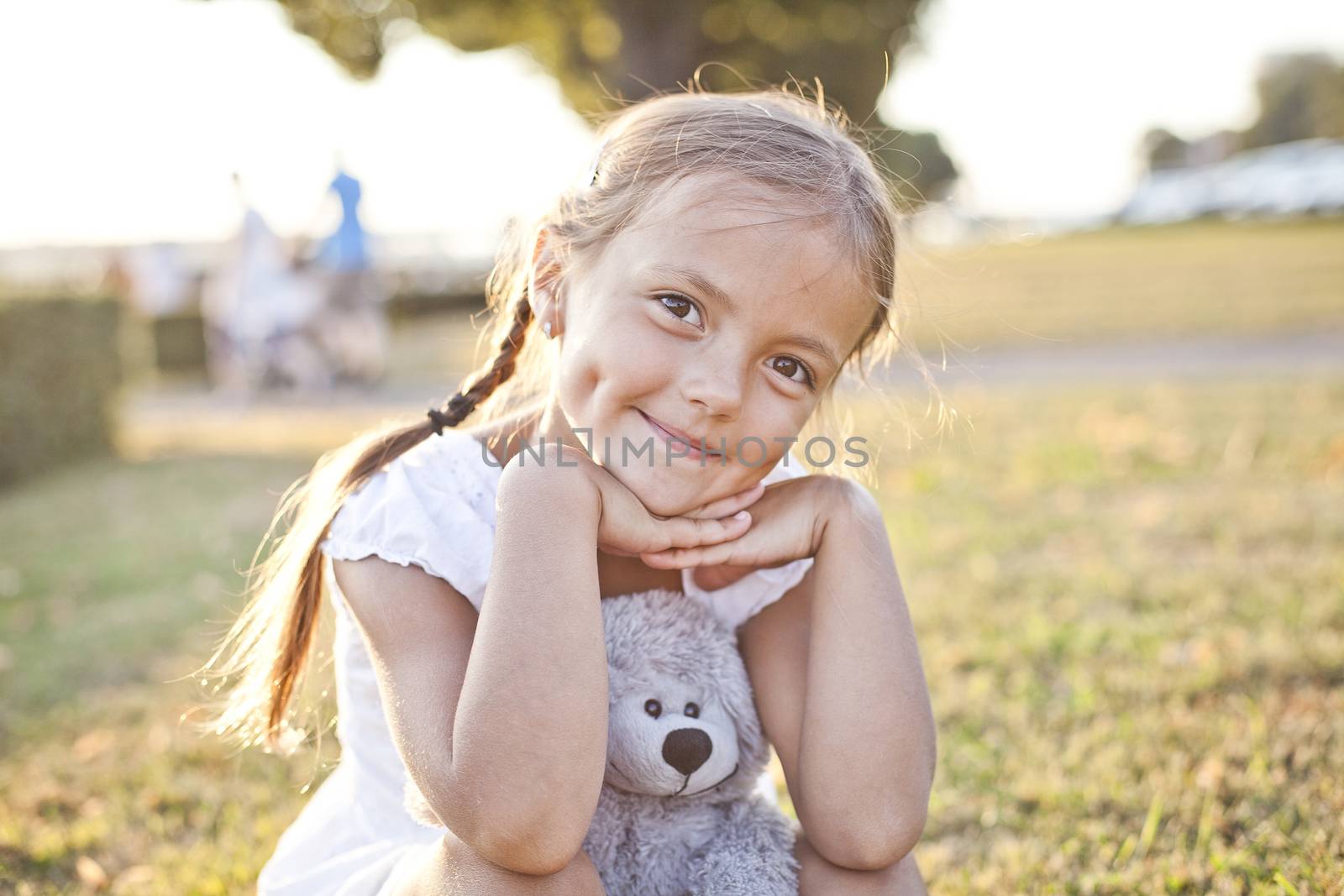 Young girl sit on a grass in a park with her toy teddy bear