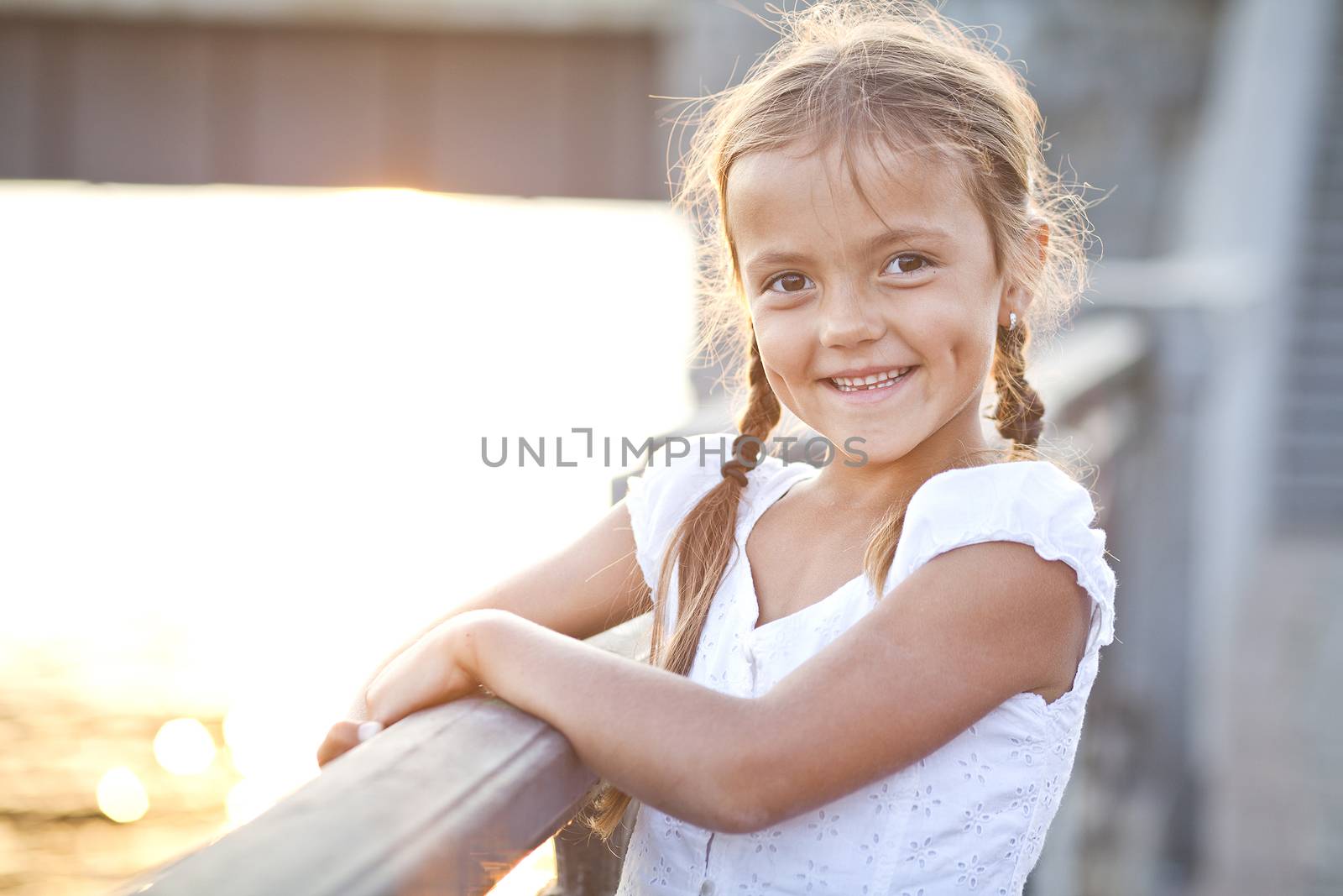Smiling child standing on a city river embankment railing