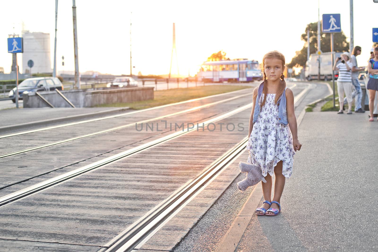 Small girl standing on a tram station with her toy teddy bear