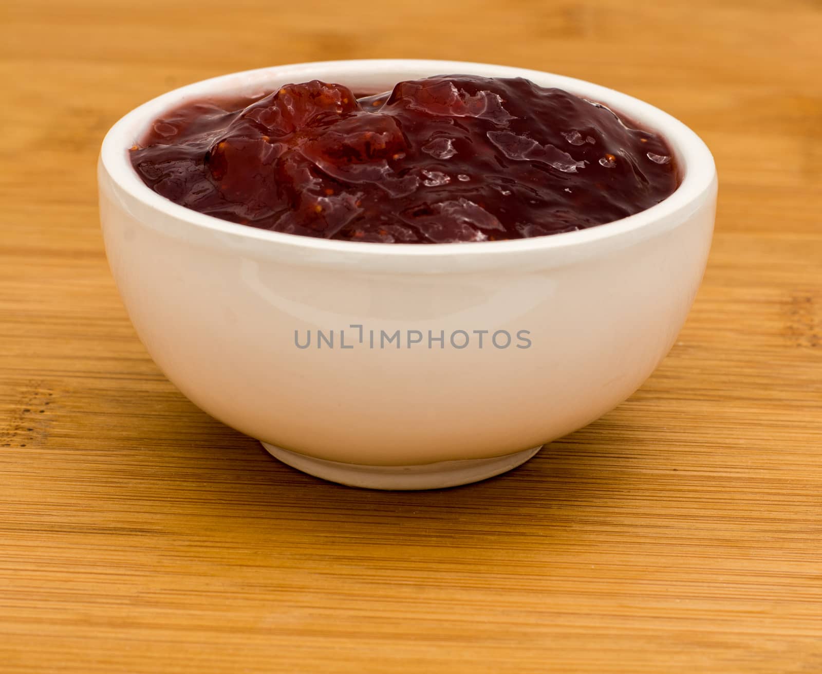 Small white pot of strawberry Jam on a wooden board