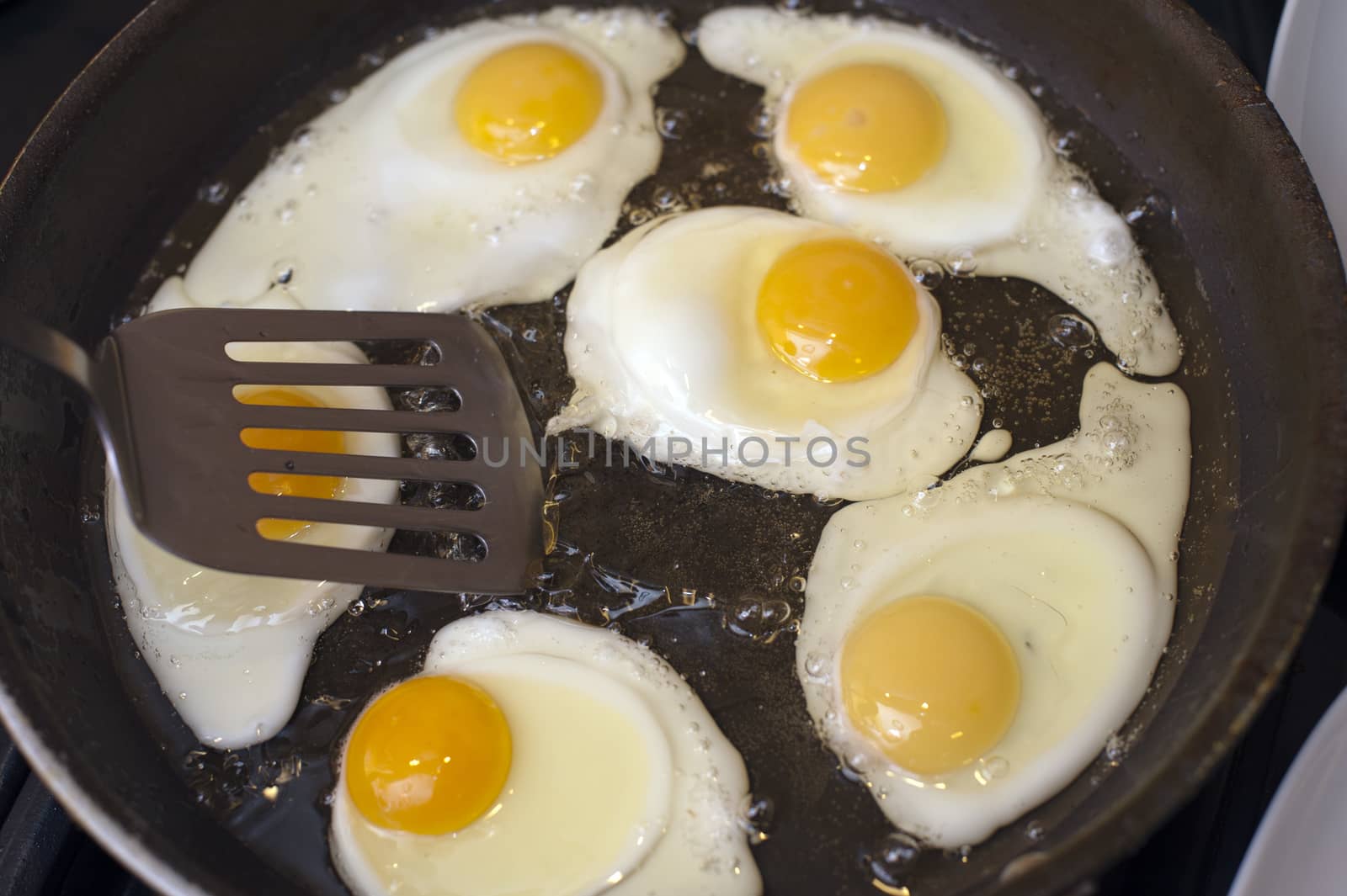 Frying a batch of eggs for breakfast in a non-stick frying pan using a spatula, close up high angle view