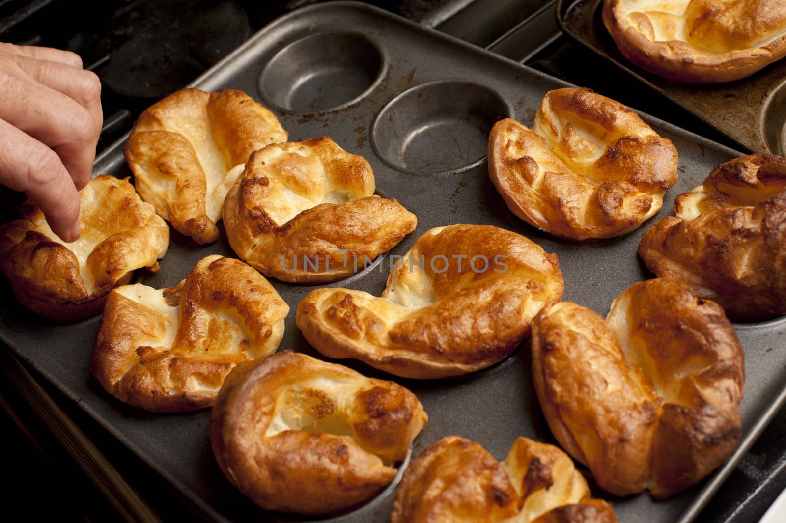 Man removing freshly baked individual fluffy golden Yorkshire puddings from a baking tray