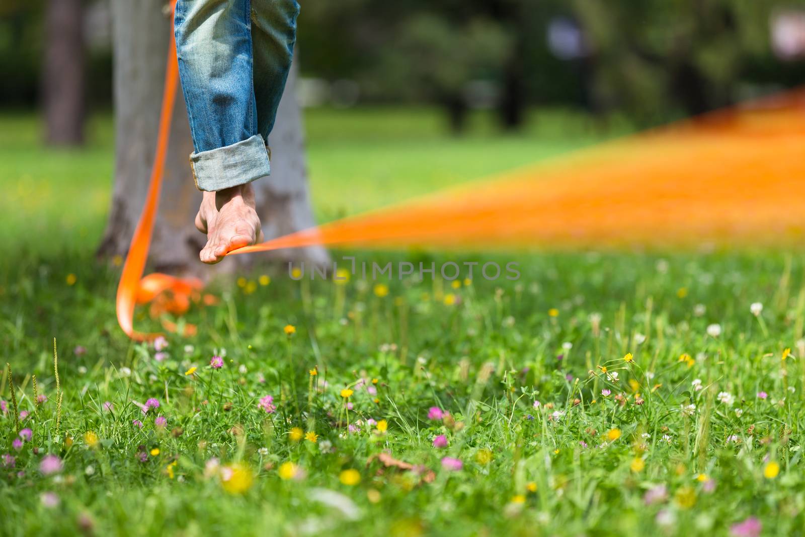 Guy practising slack line in the city park. Slacklining is a practice in balance that typically uses nylon or polyester webbing tensioned between two anchor points.