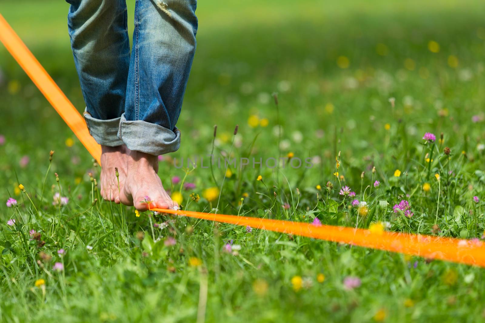 Guy practising slack line in the city park. Slacklining is a practice in balance that typically uses nylon or polyester webbing tensioned between two anchor points.