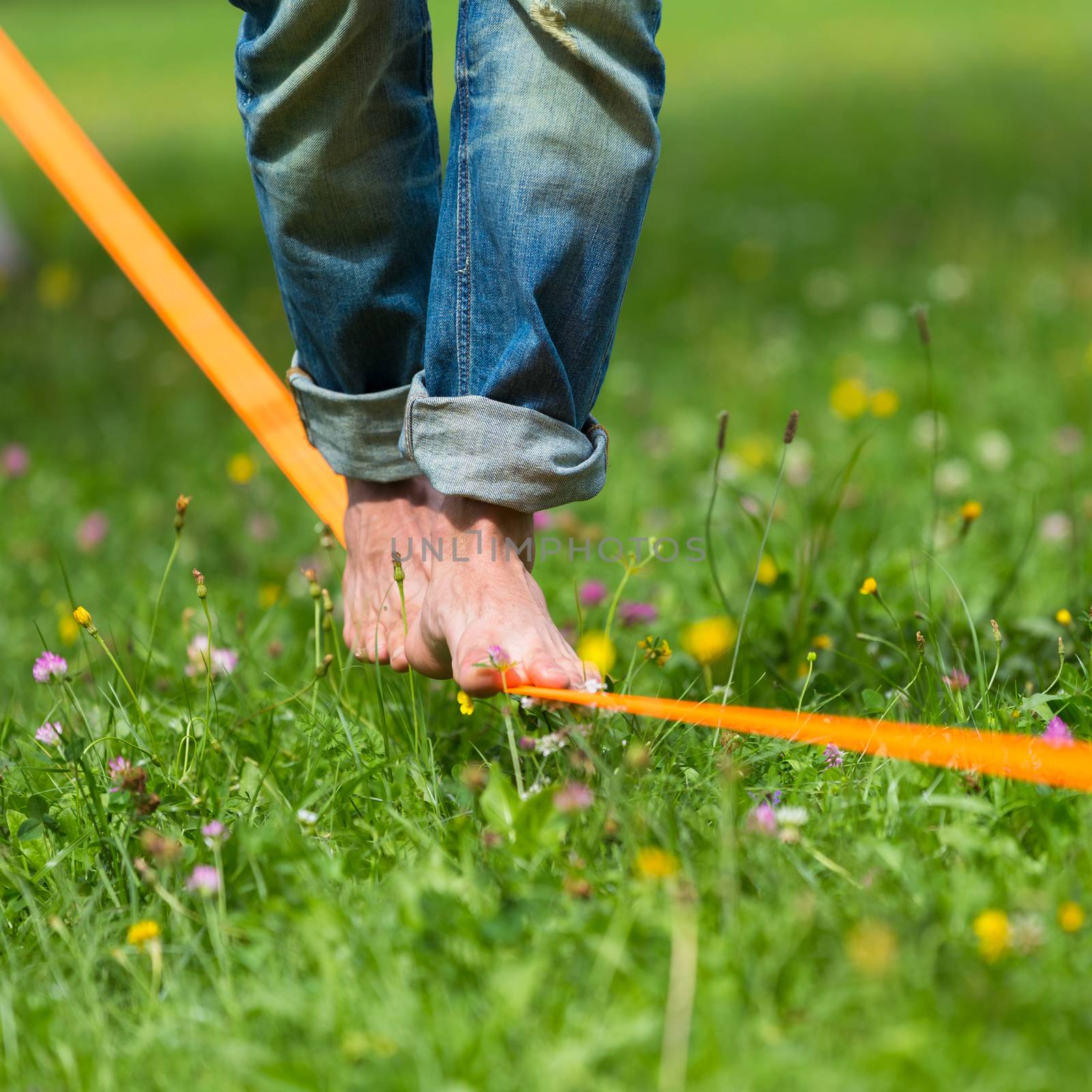 Guy practising slack line in the city park. Slacklining is a practice in balance that typically uses nylon or polyester webbing tensioned between two anchor points.