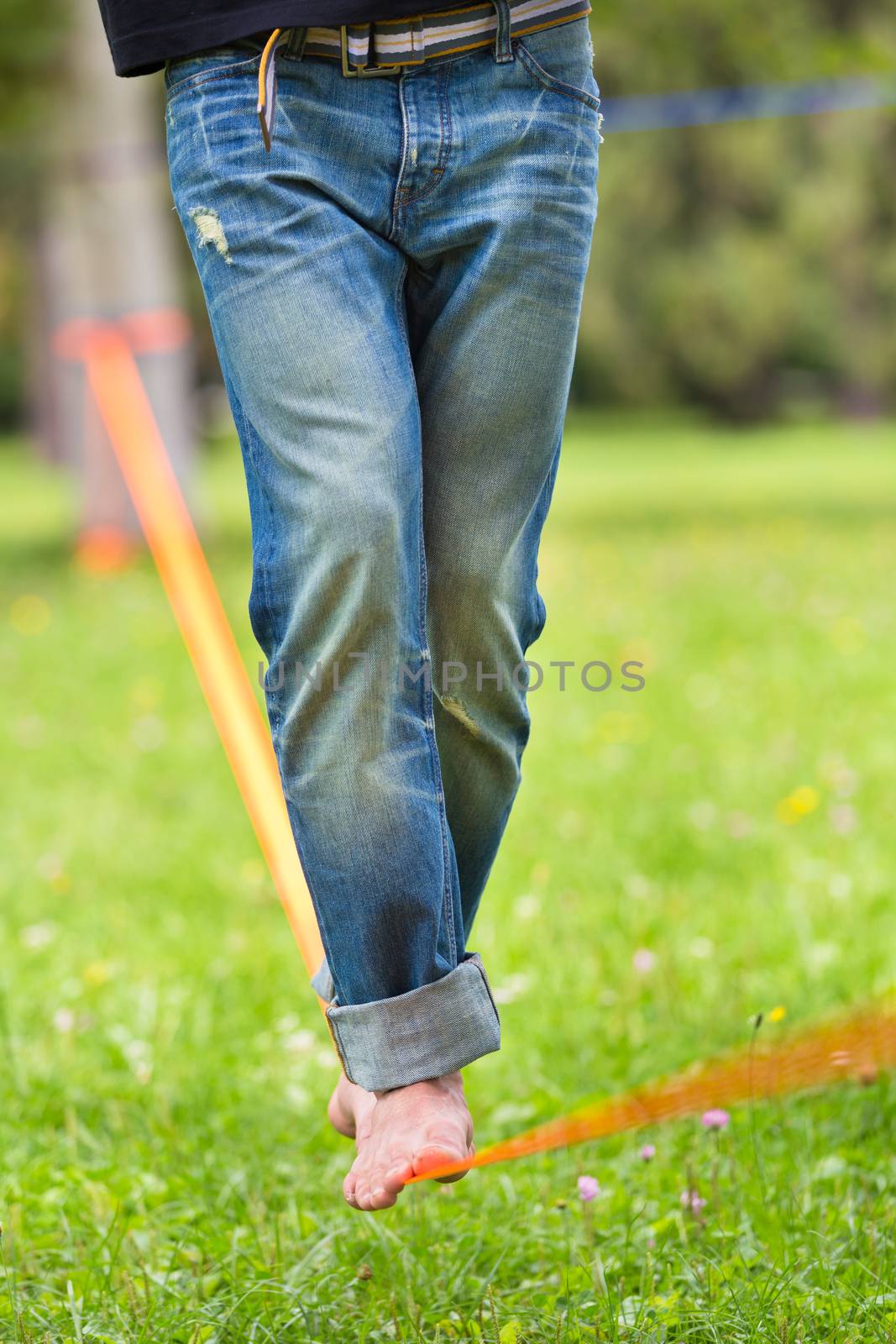 Guy practising slack line in the city park. Slacklining is a practice in balance that typically uses nylon or polyester webbing tensioned between two anchor points.