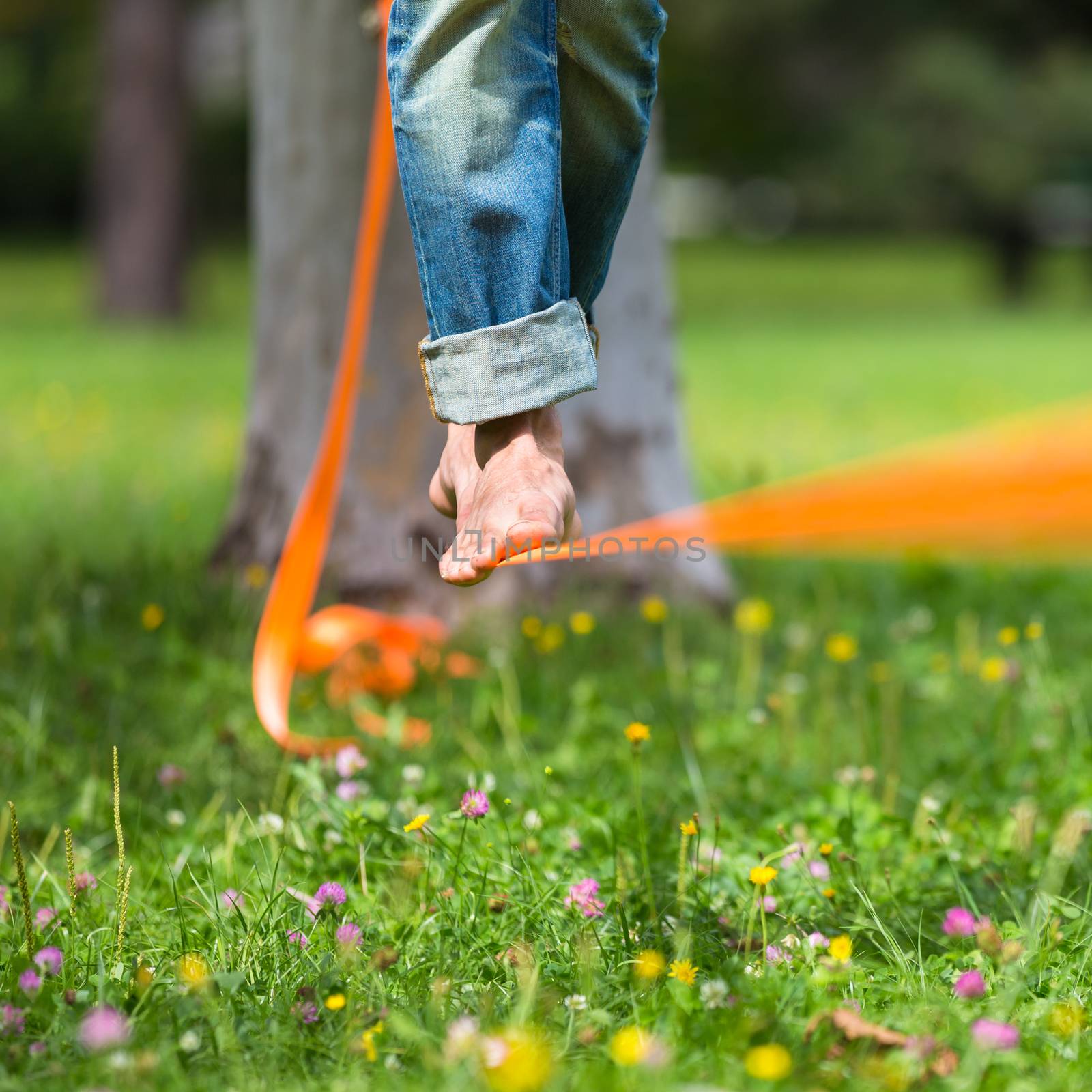 Guy practising slack line in the city park. Slacklining is a practice in balance that typically uses nylon or polyester webbing tensioned between two anchor points.