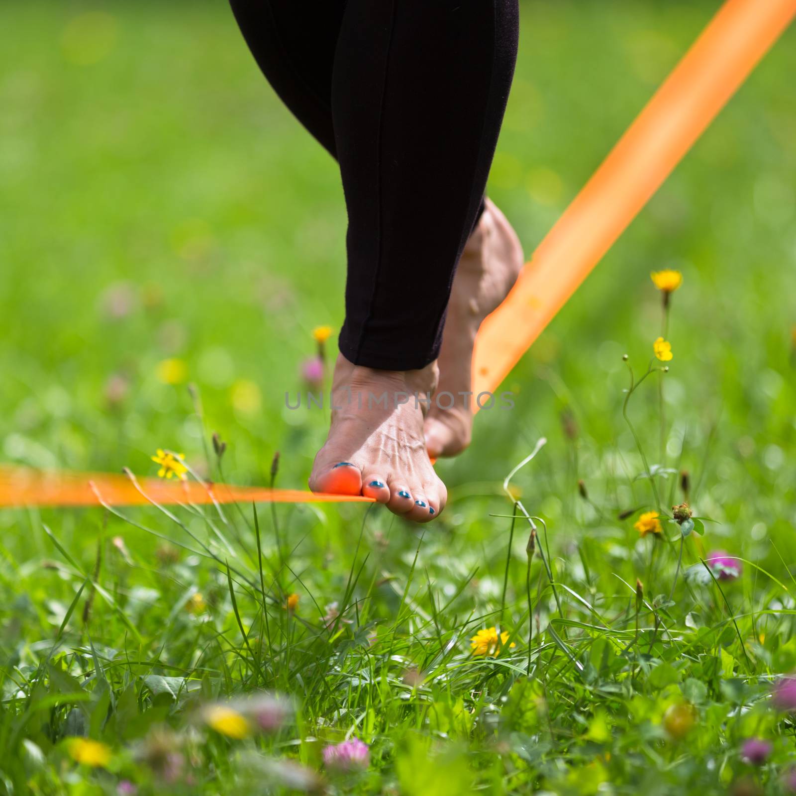 Lady practising slack line in the city park. Slacklining is a practice in balance that typically uses nylon or polyester webbing tensioned between two anchor points.