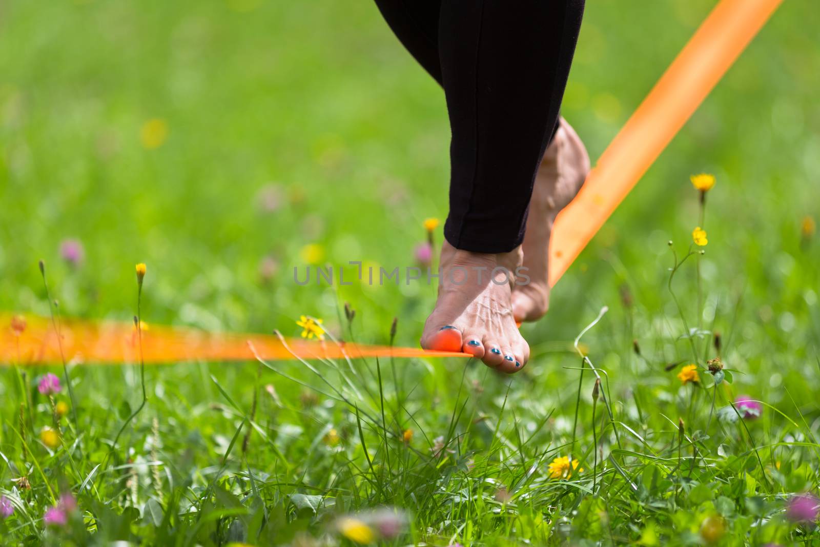 Lady practising slack line in the city park. Slacklining is a practice in balance that typically uses nylon or polyester webbing tensioned between two anchor points.
