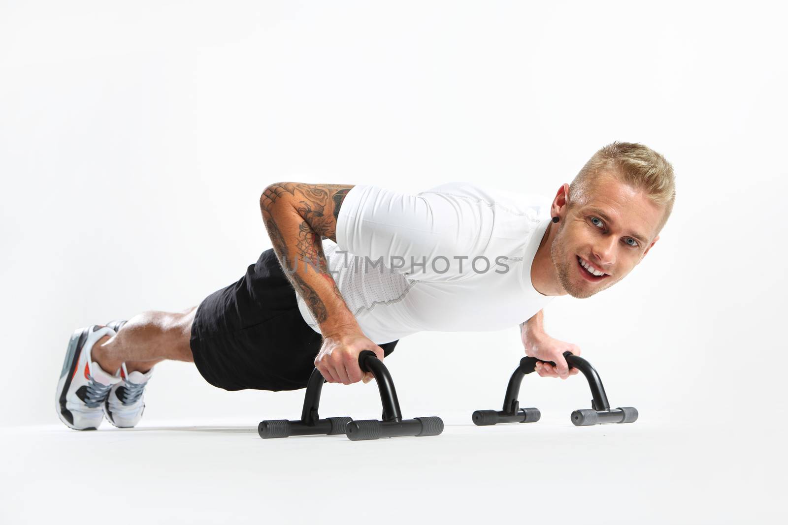 Attractive young man doing push-ups, tattooed in sports trousers