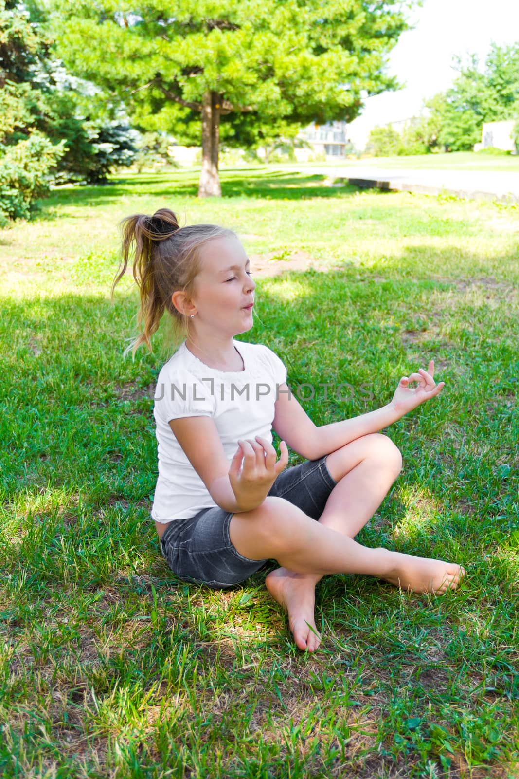 Cute girl are sitting on green grass in lotus pose