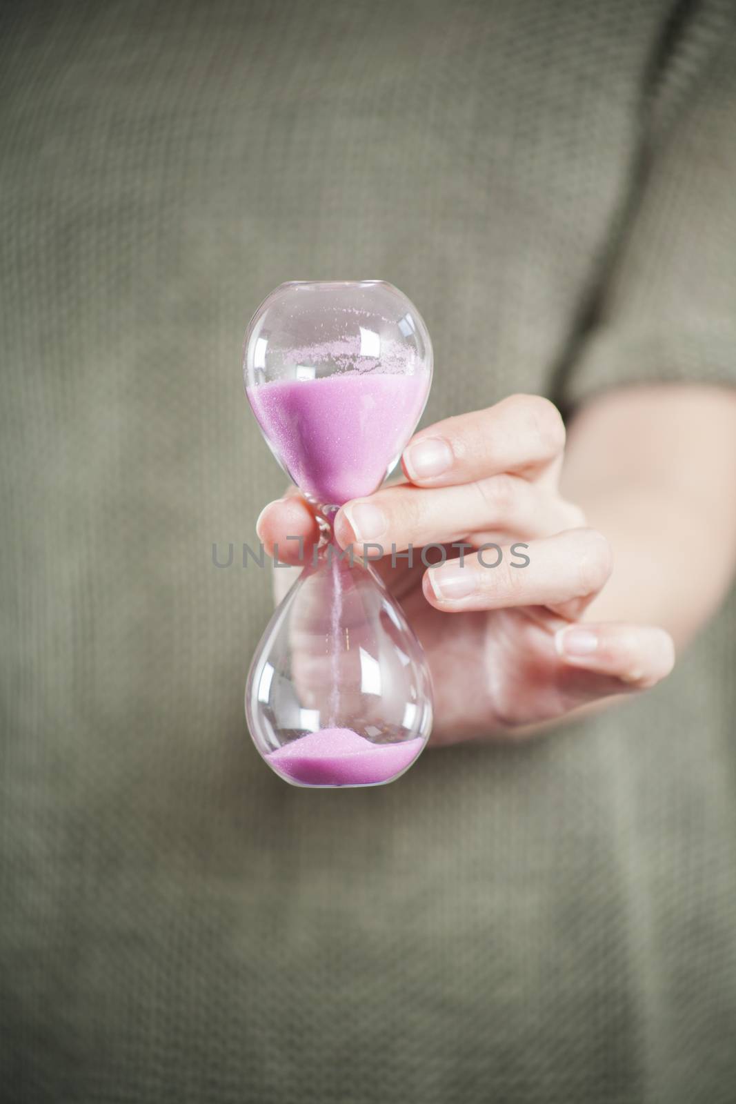 pink sand clock in woman hands over green background