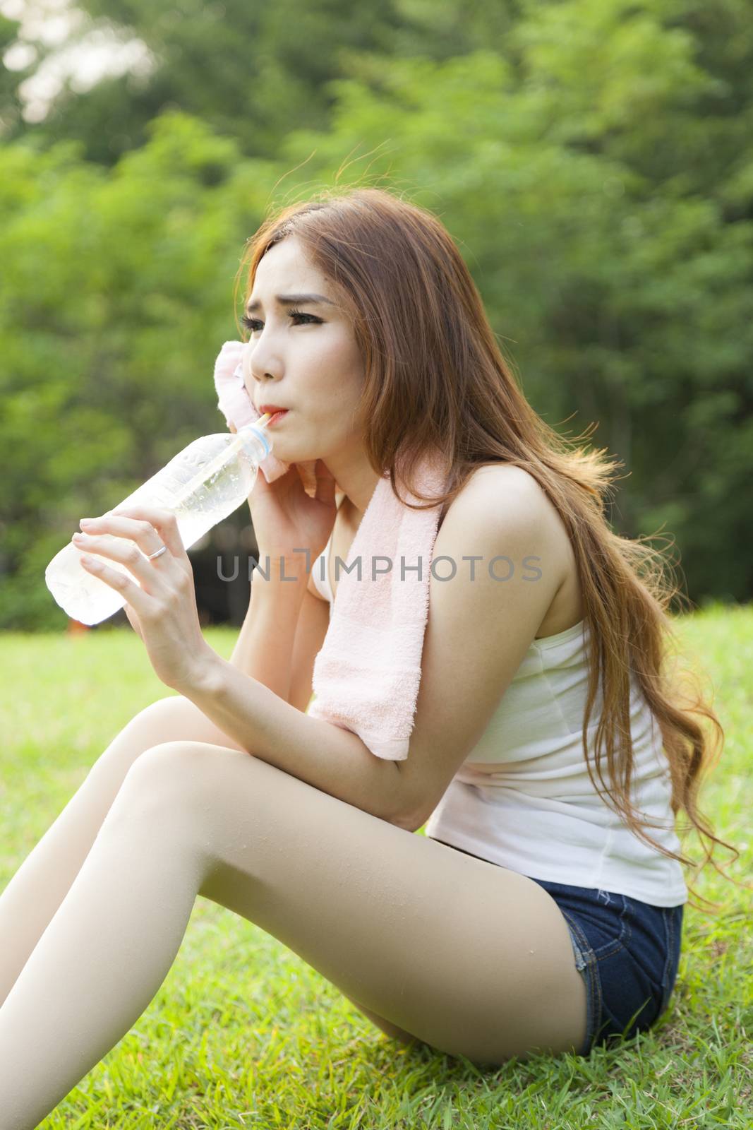 Woman sit and drink after exercise. On the lawn after a workout in the park.
