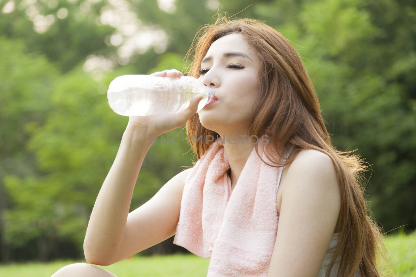 Woman sit and drink after exercise. On the lawn after a workout in the park.