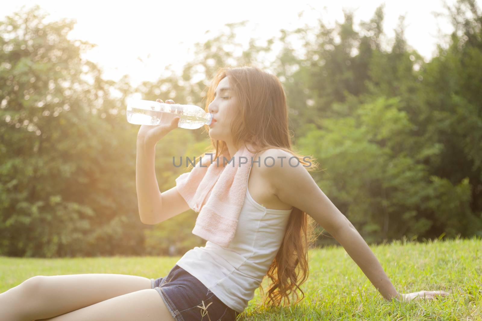 Woman sit and drink after exercise. On the lawn after a workout in the park.