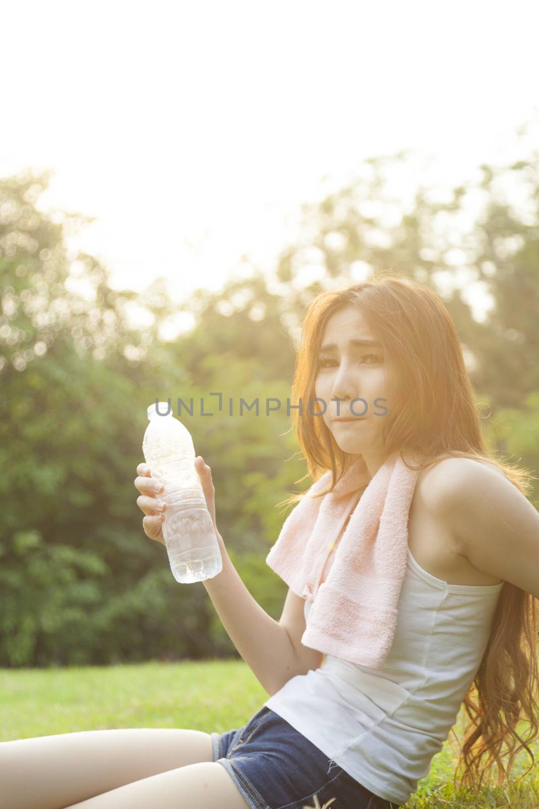 Woman sitting rest after exercise. Hand holding a bottle of water and sit On the lawn.