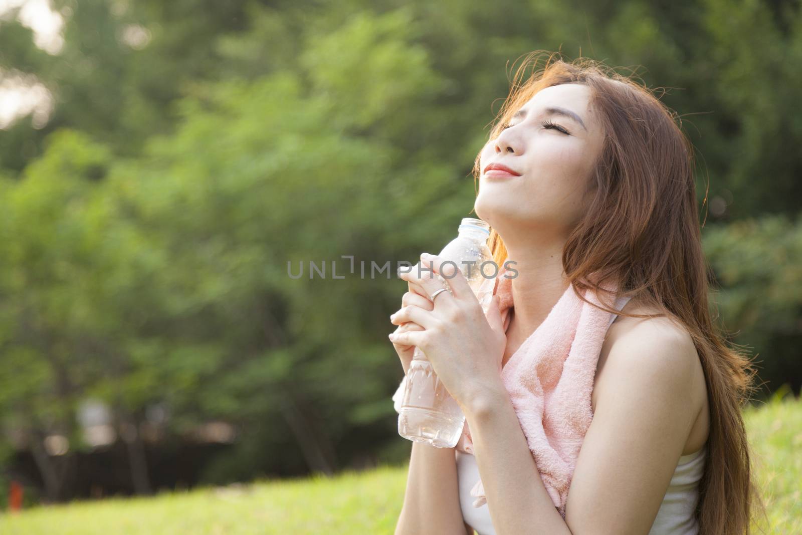 Woman sitting rest after exercise. Hand holding a bottle of water and sit On the lawn.