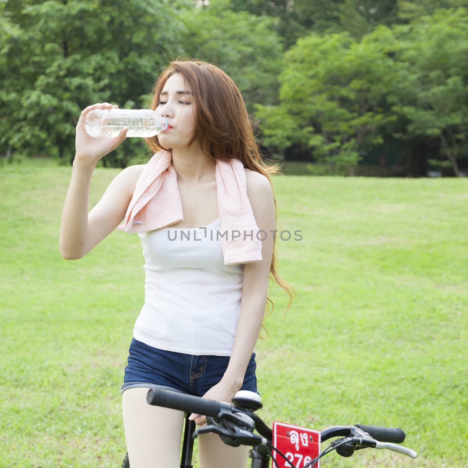 Woman drinking water. Bike ride on grass in the park.