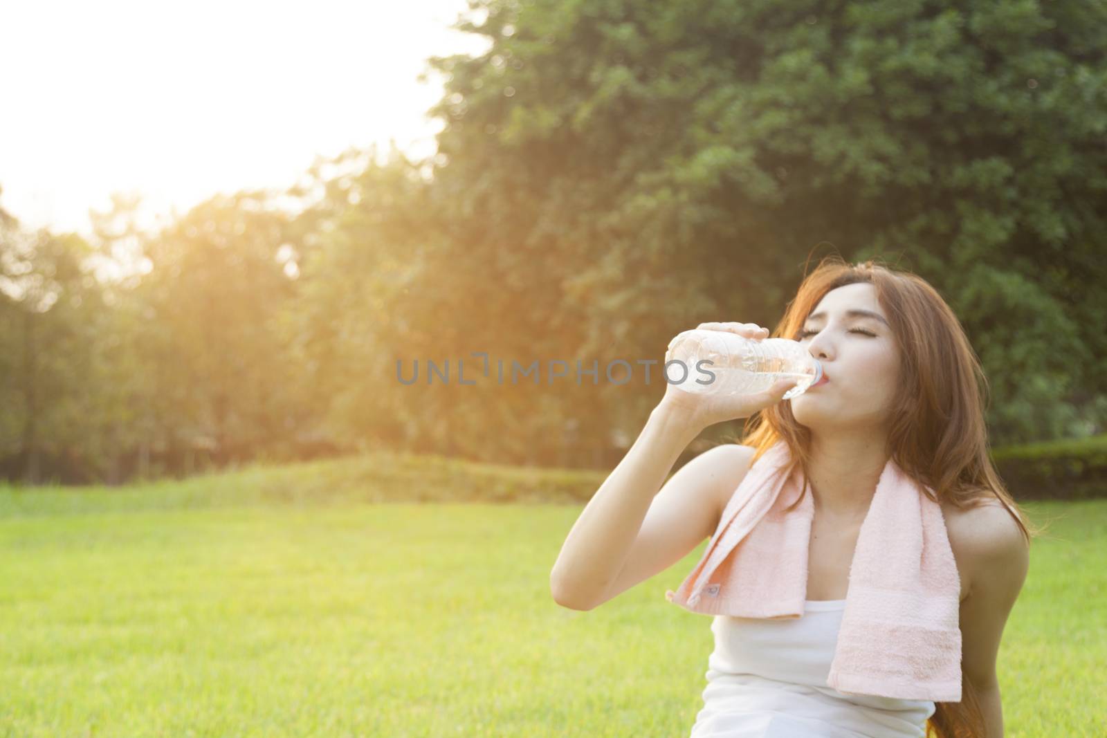 Woman drinking water and sit on grass. After jogging in the evening.