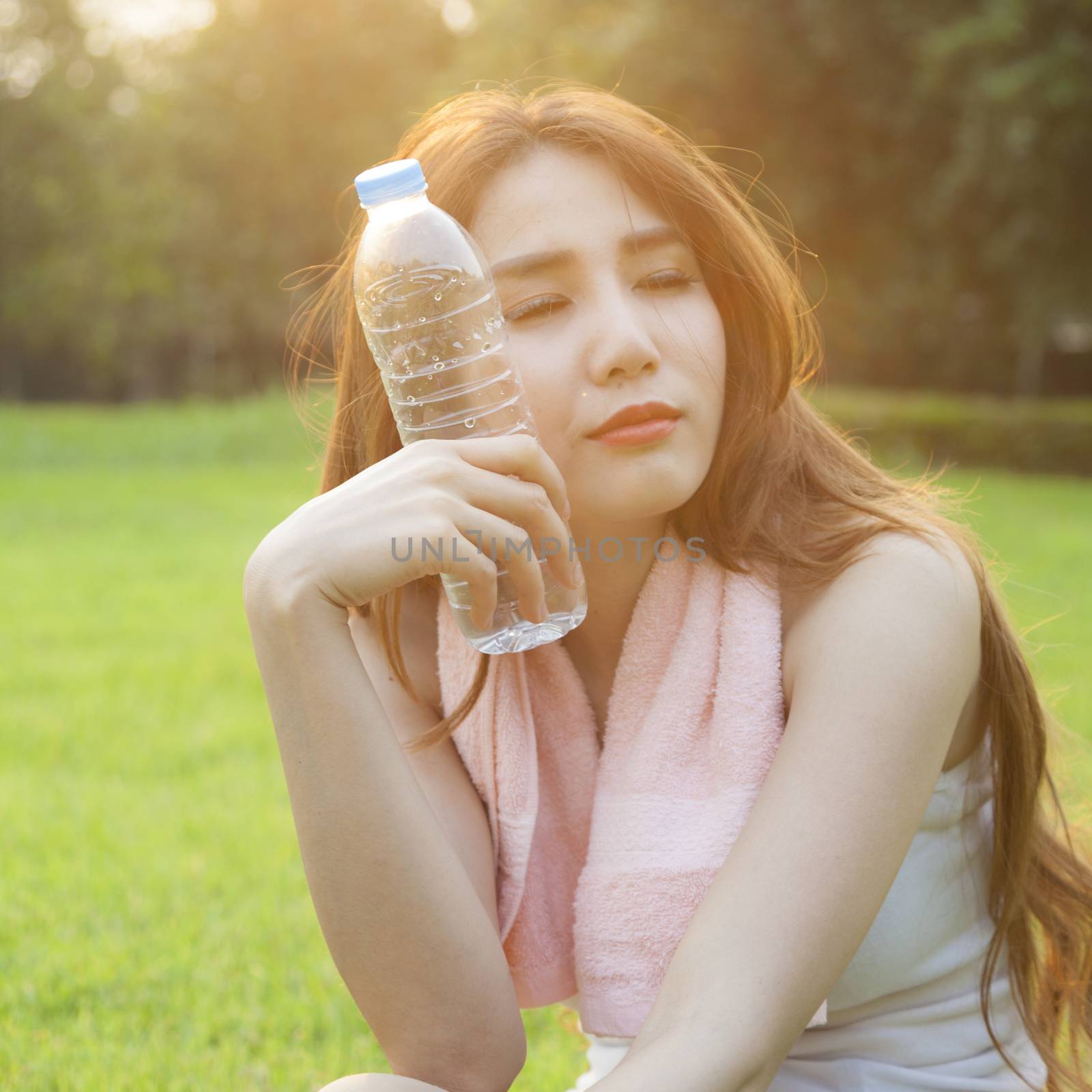 Woman Sitting and holding a bottle of water. Sitting on grass in the park after jogging. In the evening