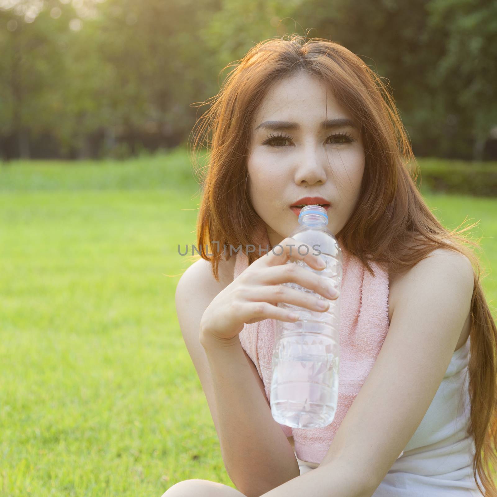 Woman drinking water and sit on grass. After jogging in the evening.