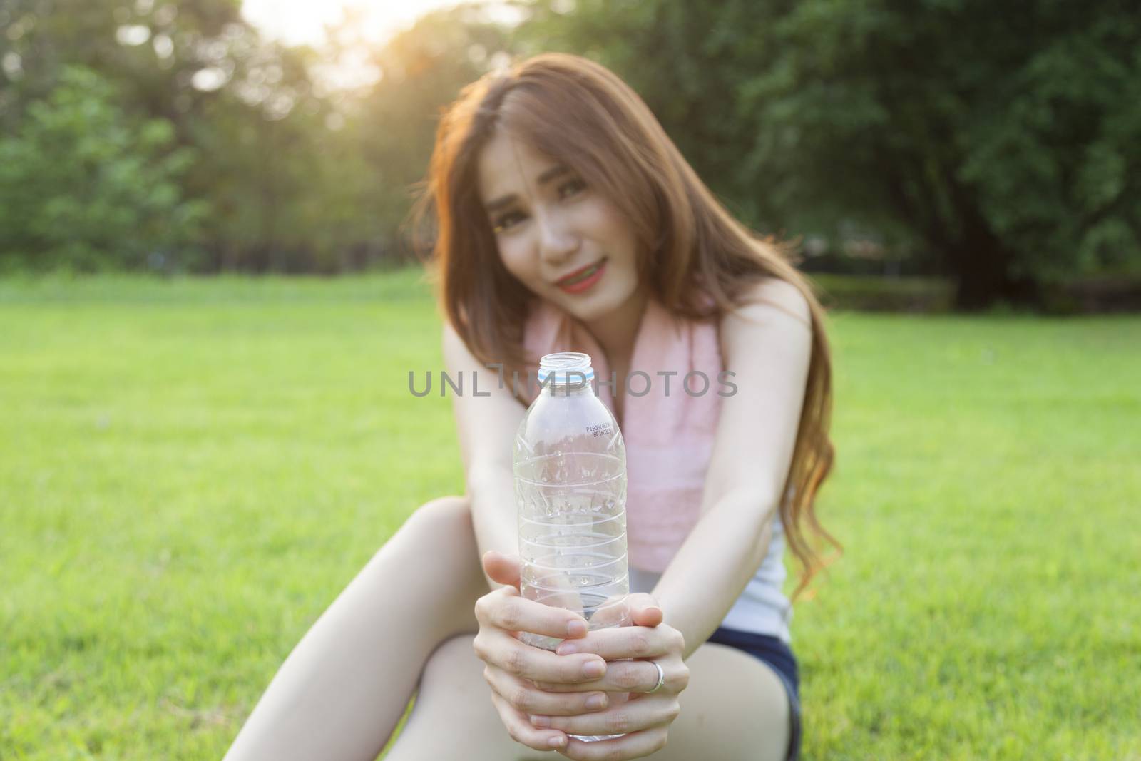 Woman holding a bottle of water and handed it to. Sitting on the lawn after jogging.