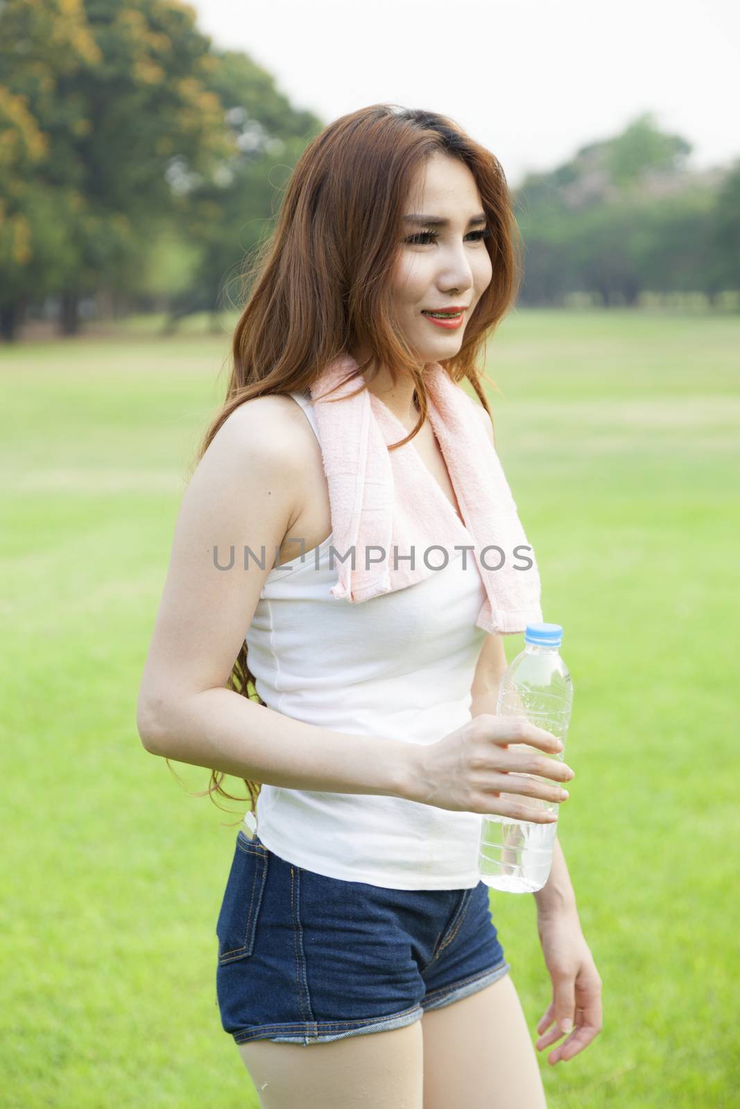 Woman standing breaks and drink water after jogging on grass in the park.