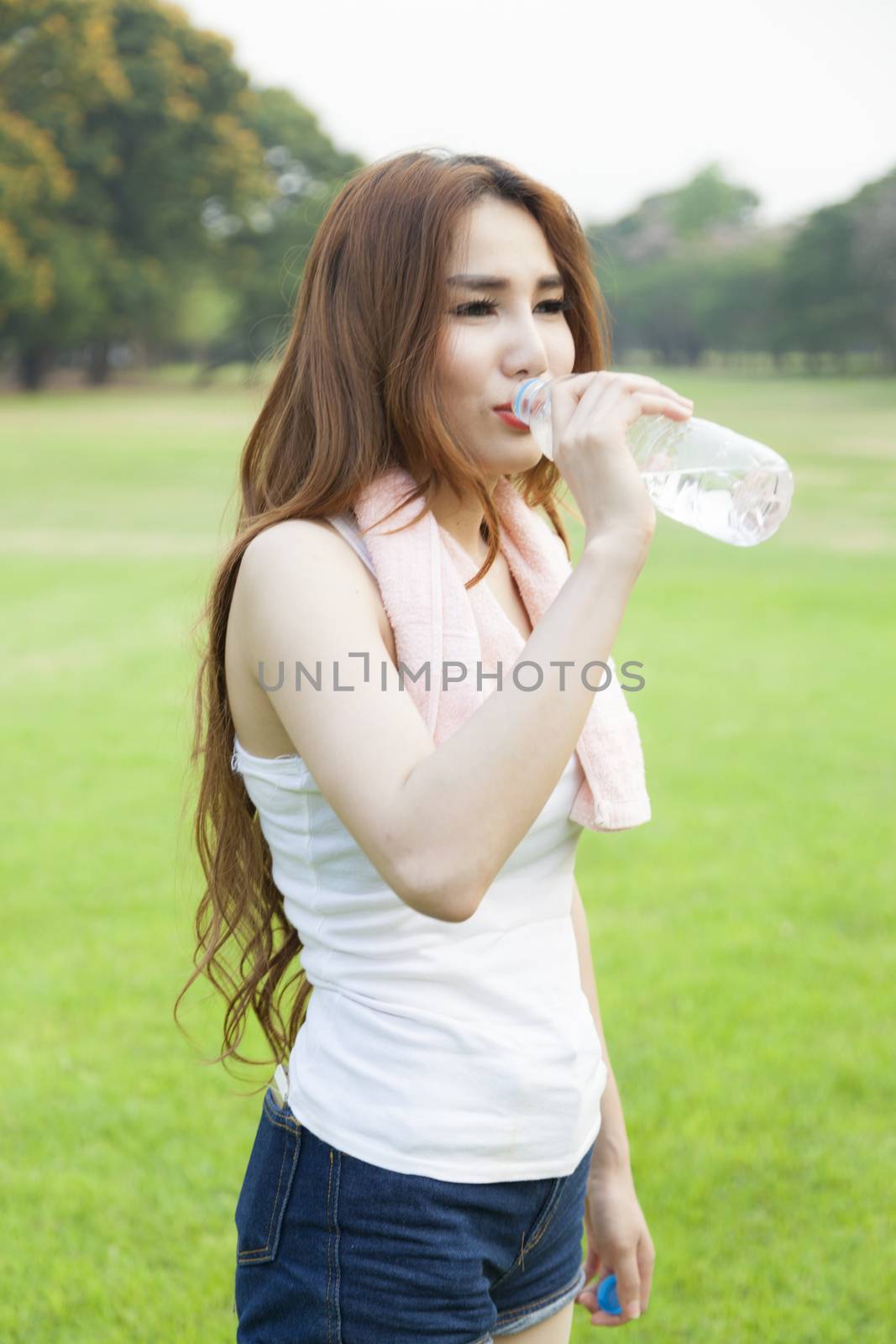 Woman standing breaks and drink water after jogging on grass in the park.