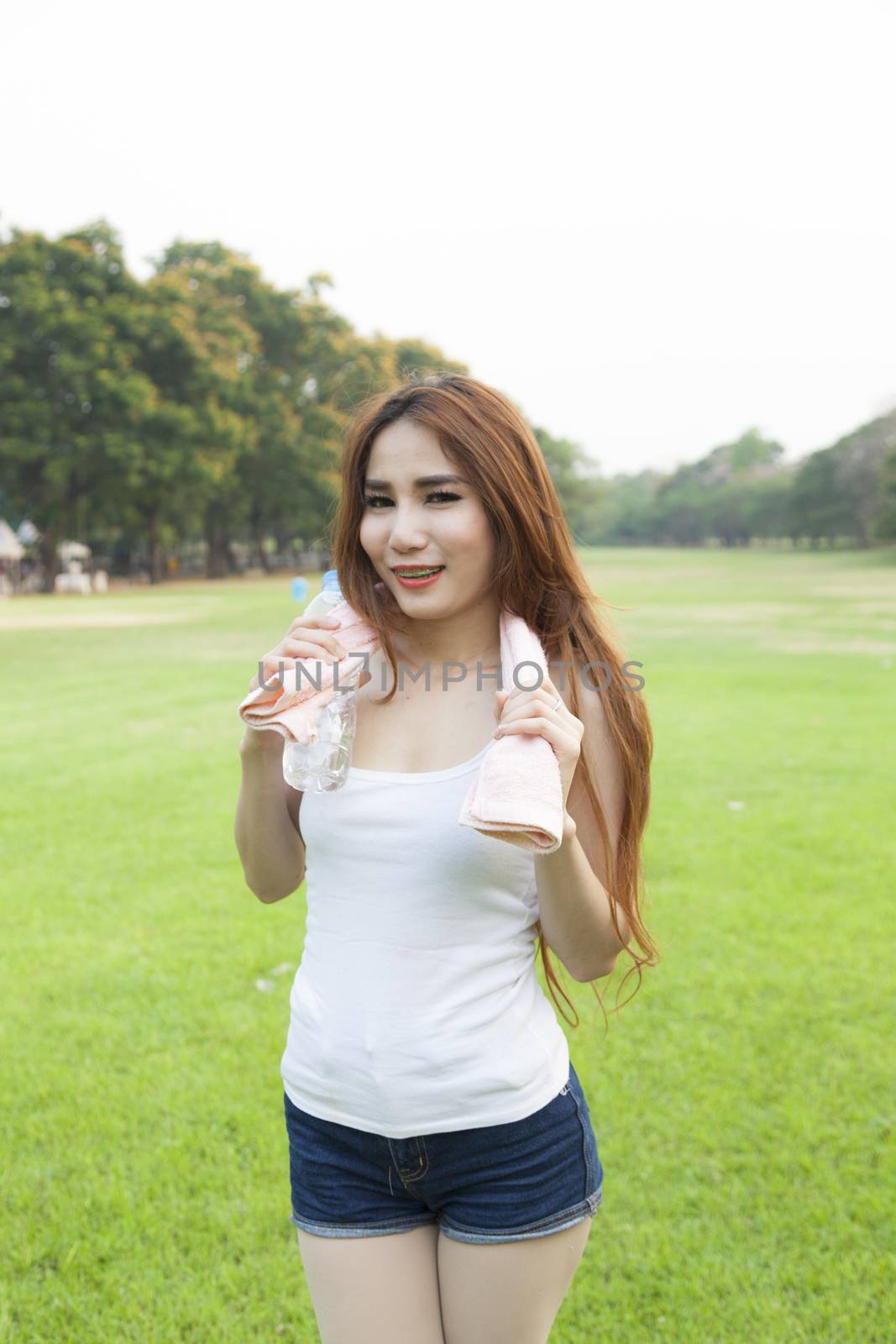 Woman holding a bottle of water. Jogging on grass in the park.