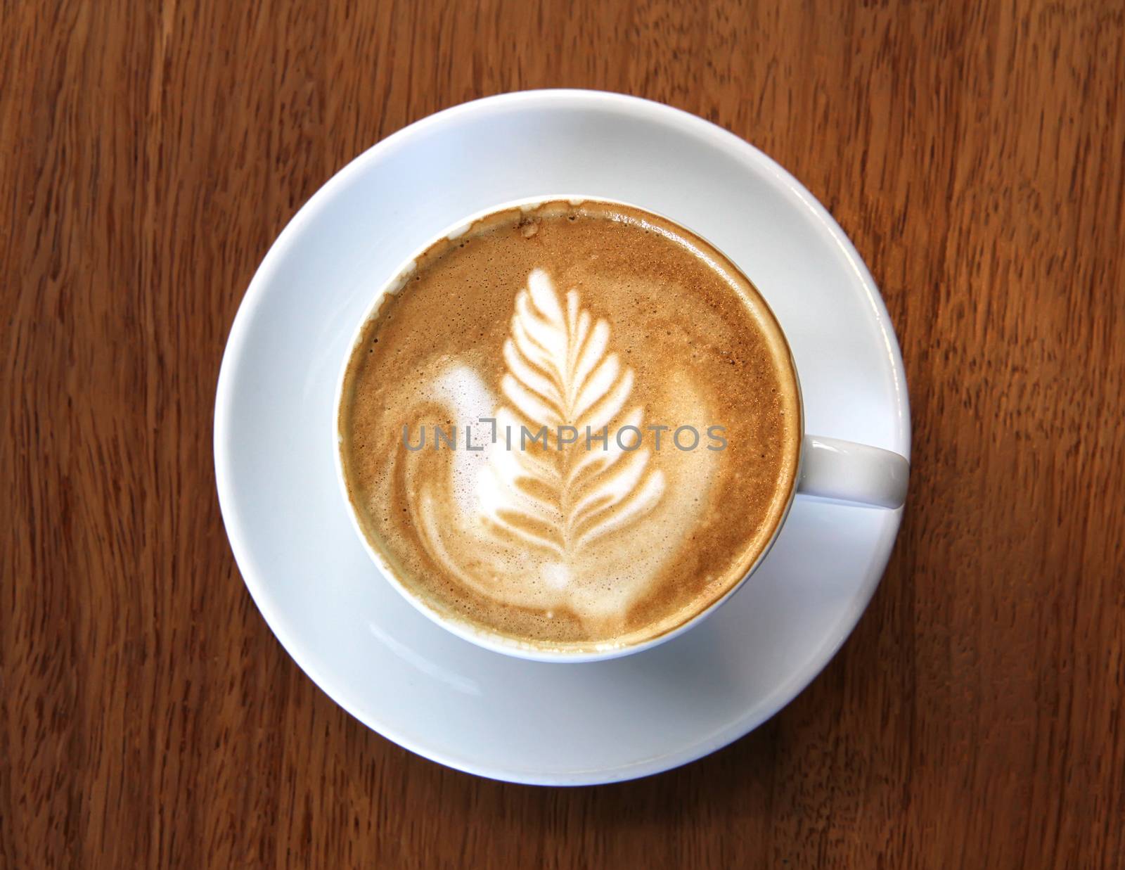 Cup of coffee latte with leaf design art in froth, on a wooden table and viewed from top.