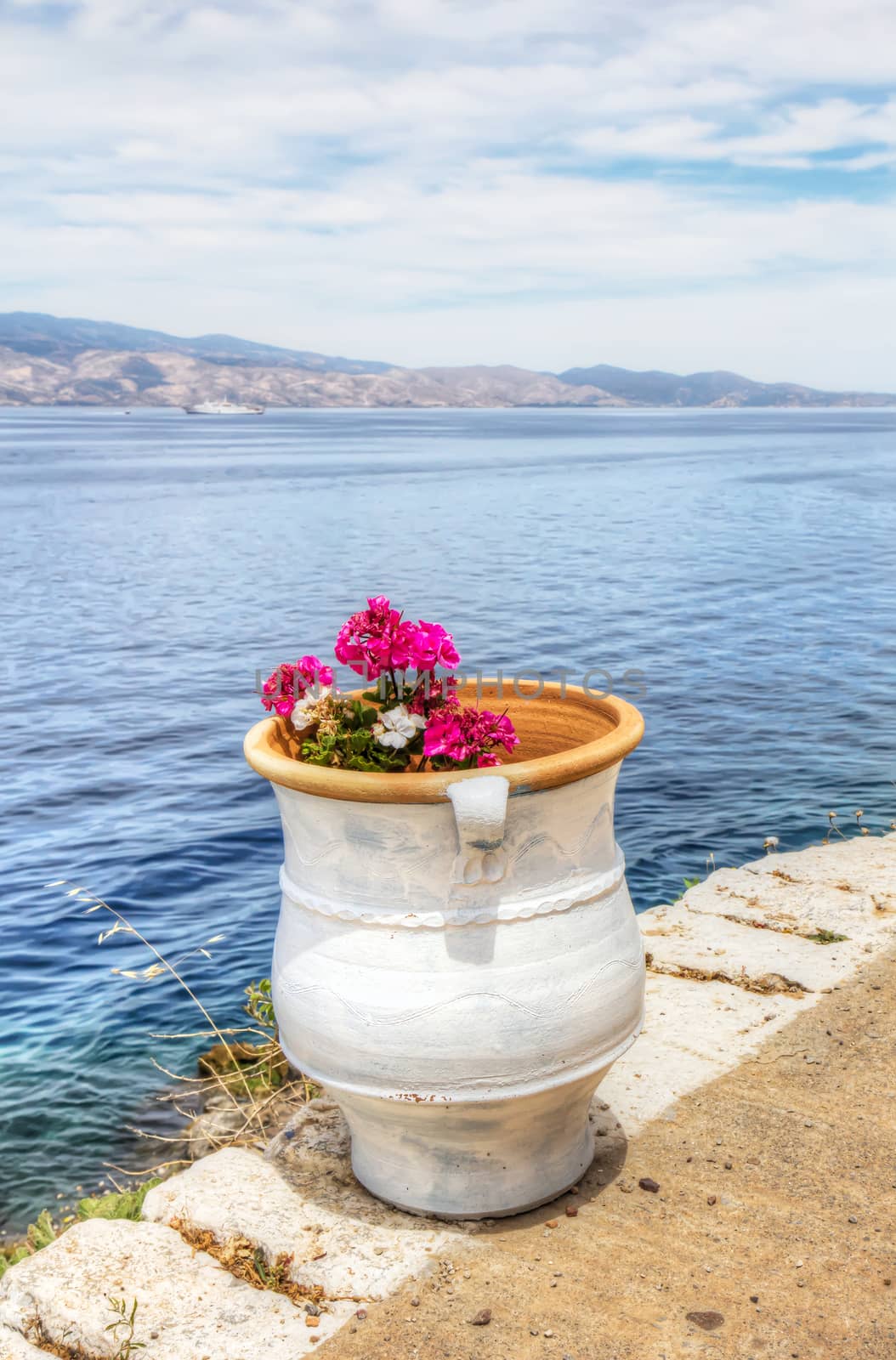 Colourful pink and white flowers in white clay pot overlooking the Saronic Gulf in Hydra island in the Aegean Sea, Greece.