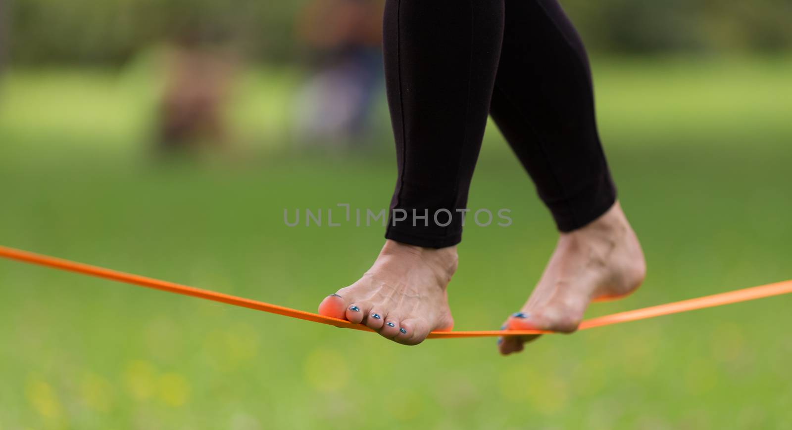 Lady practising slack line in the city park. Slacklining is a practice in balance that typically uses nylon or polyester webbing tensioned between two anchor points.