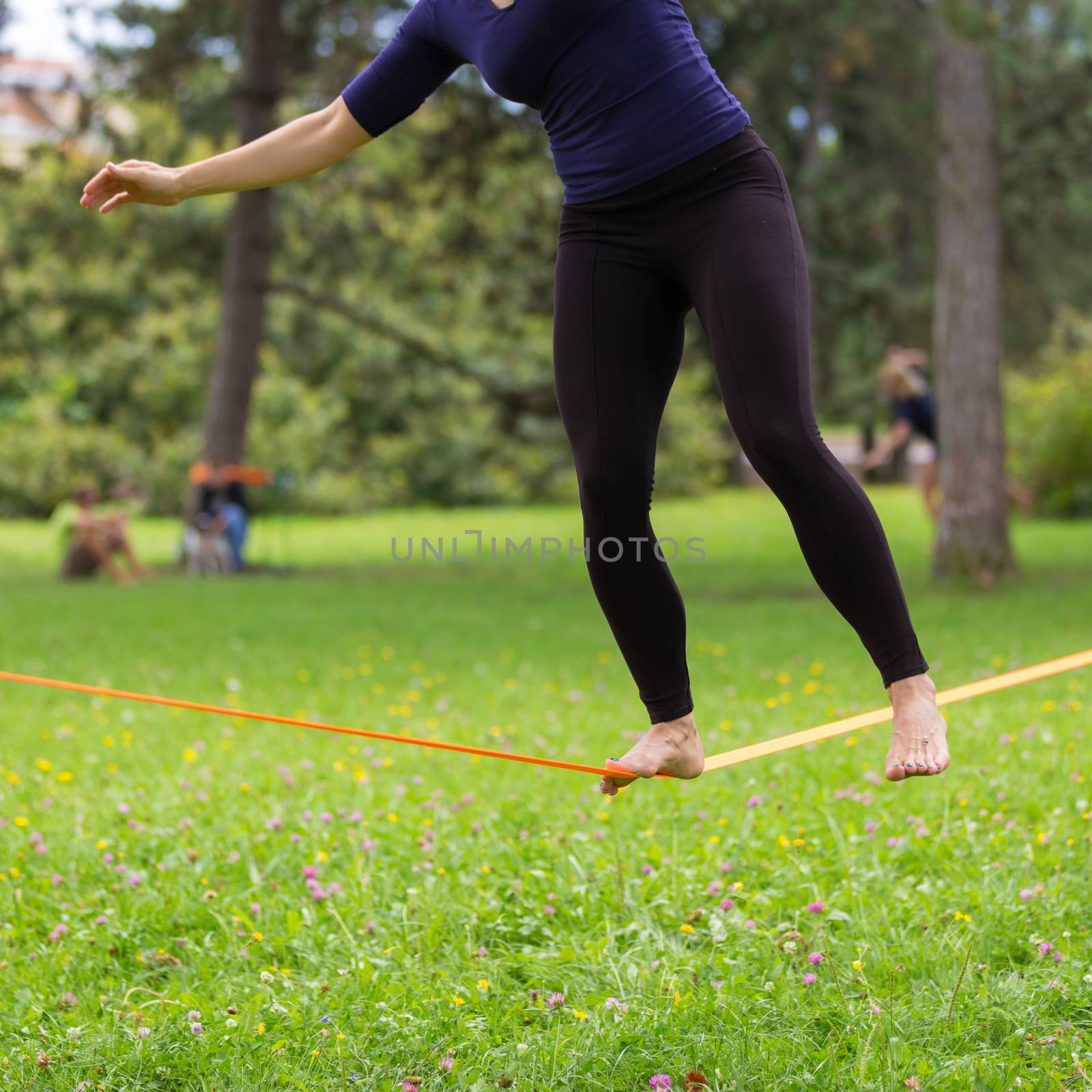 Lady practising slack line in the city park. Slacklining is a practice in balance that typically uses nylon or polyester webbing tensioned between two anchor points.