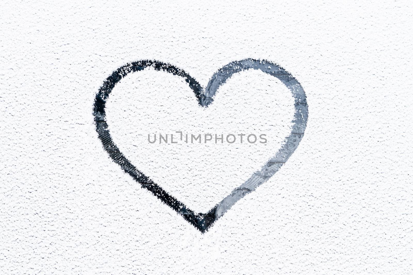 Heart drawn on a glass covered with fresh Christmas snow.